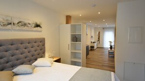 Um quarto com cabeceira estofada, cama com roupa de cama branca e uma estante embutida.