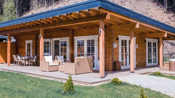 A wooden cabin with a covered patio, outdoor seating, and a hot tub. - Chalet Bischofsmühle (Helmbrechts)