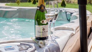 A hot tub with a bottle of champagne and glasses on a table, surrounded by a natural landscape. - Chalet Bischofsmühle (Helmbrechts)