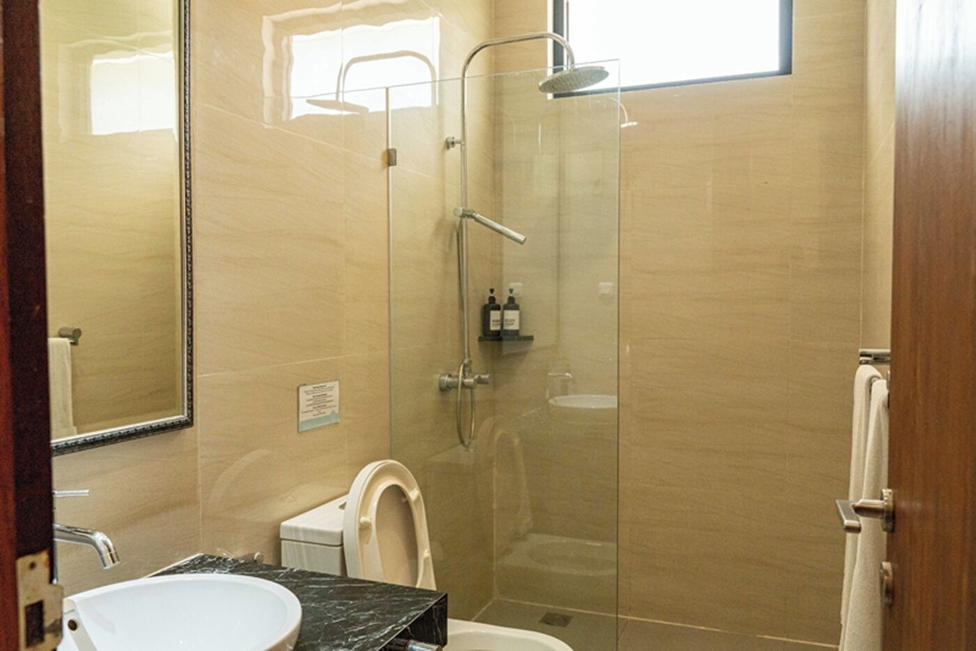 Un baño con ducha de vidrio, inodoro, lavamanos con encimera de mármol y espejo.