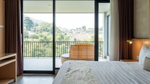 A bedroom with a large bed, a chair, a nightstand, and a view of a balcony with a railing.