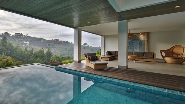 A modern infinity pool with a clear view of the landscape, a seating area with sofas and a patterned tapestry, and a wooden deck.