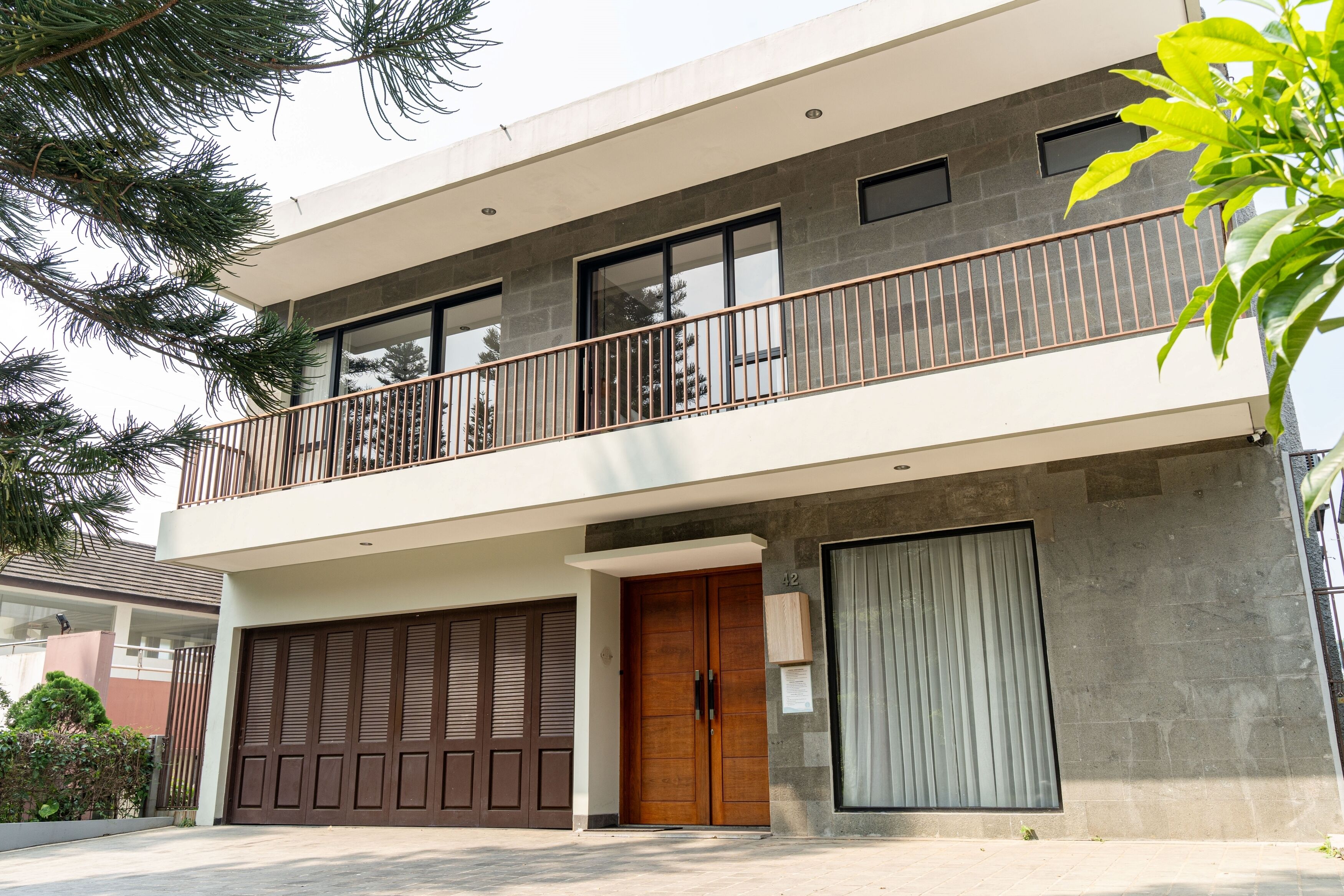 Uma casa moderna de dois andares com varanda, portas de madeira grandes e garagem.