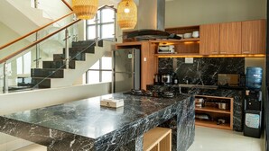 A modern kitchen with a marble countertop, wooden cabinets, a built-in oven, and a stainless steel refrigerator.