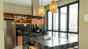 A modern kitchen with a marble island, stainless steel appliances, wooden cabinets, and large windows.