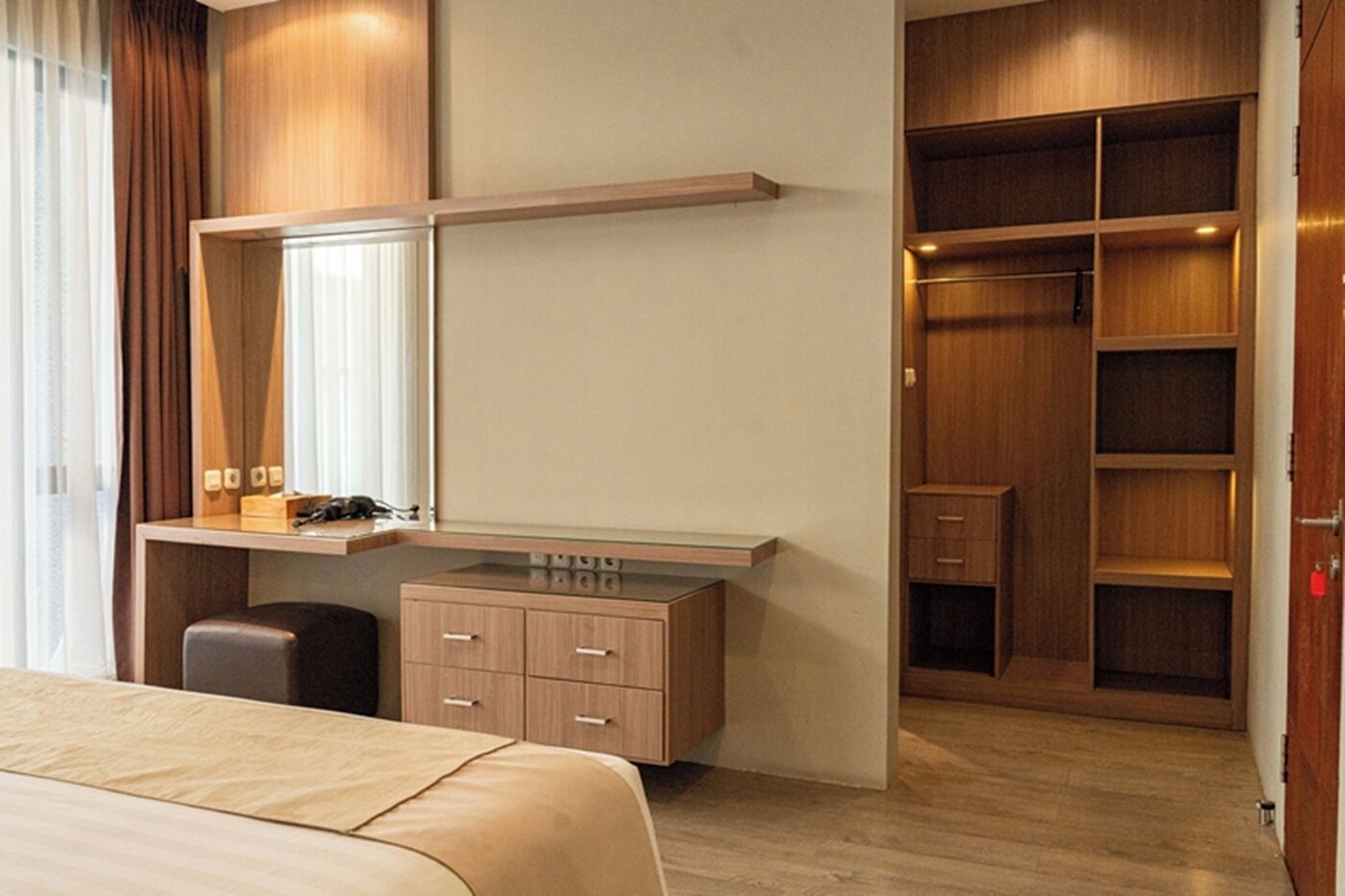 Una camera d'albergo con un letto, una scrivania con uno specchio, un armadio e una dispensa a muro.