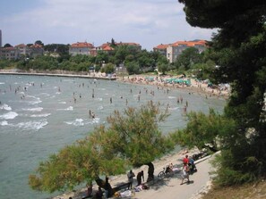 A beach with people swimming and sunbathing, surrounded by buildings and trees. - Apartments Bulovic (Split)