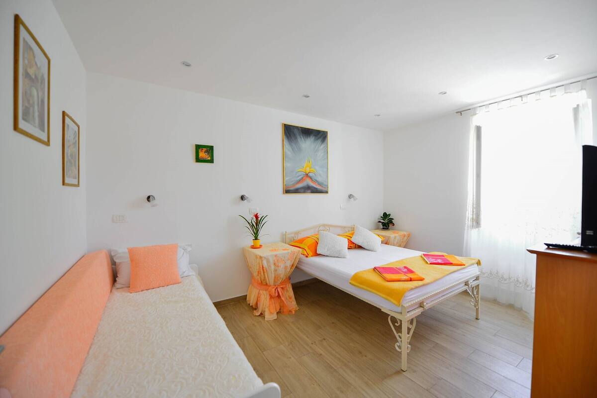 Un dormitorio con cama, sofá, una mesita con una planta y un cuadro en la pared.