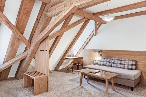 Un dormitorio tipo loft con vigas de madera a la vista, un sofá, una mesita y una silla.