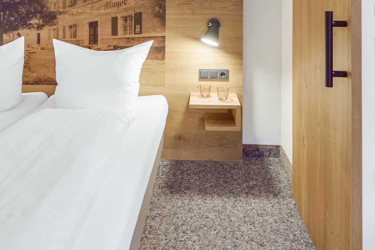 A bedroom with a bed, wooden headboard, a nightstand, a wall-mounted shelf, and a wardrobe.