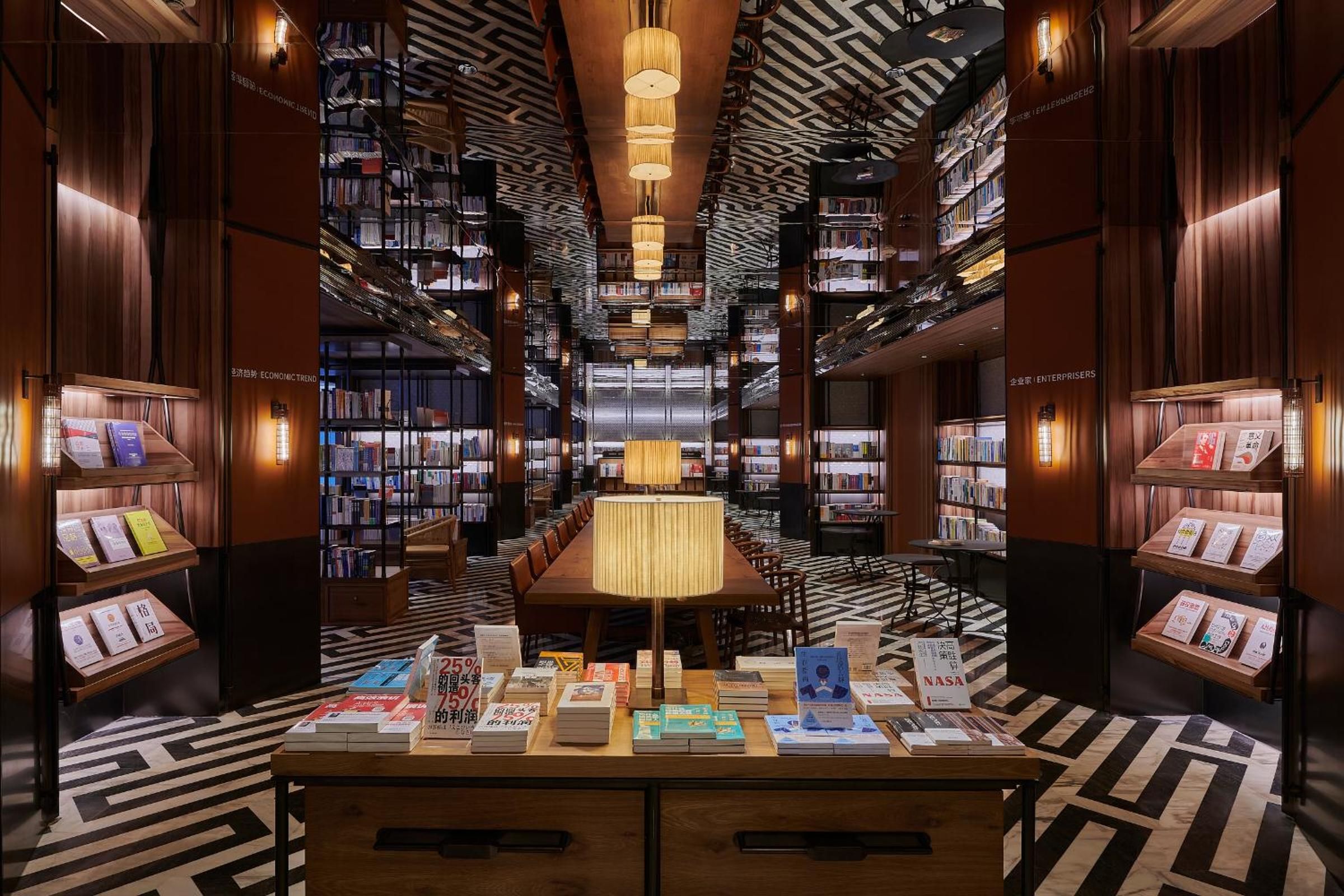 A library interior with bookshelves, a central table, and a patterned floor.
