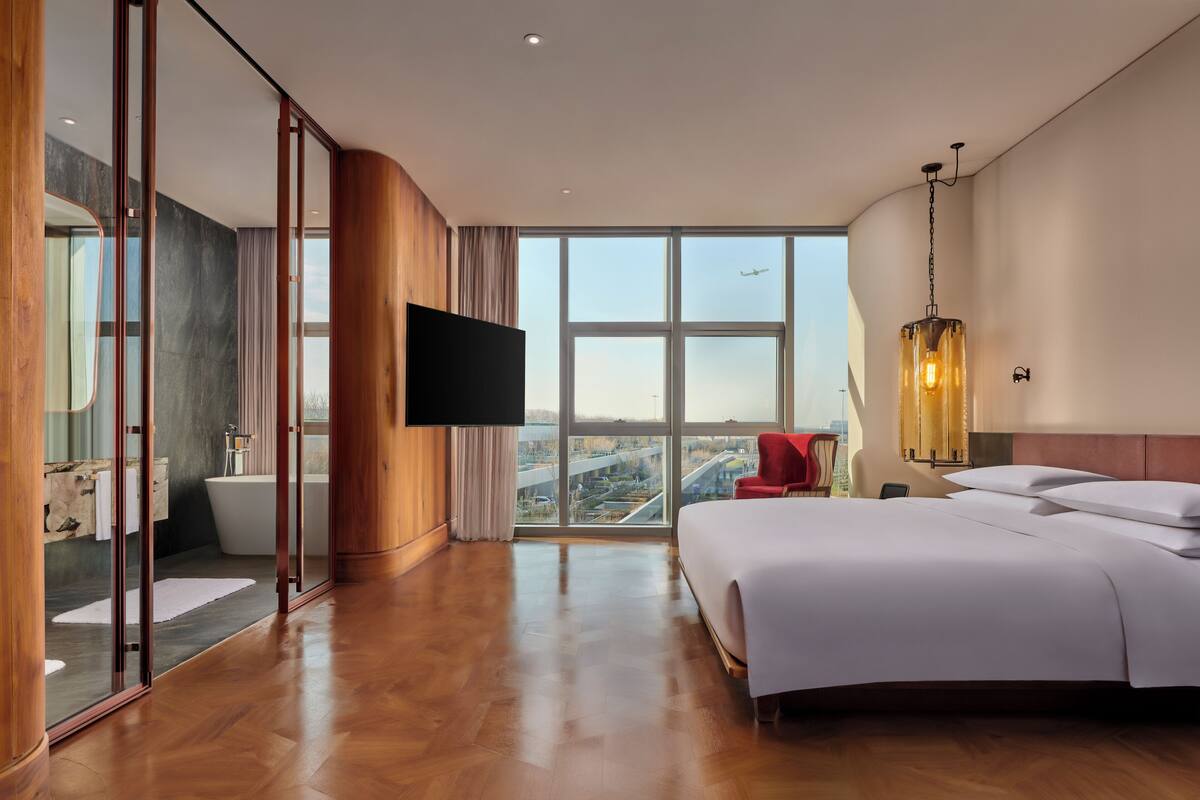 Ein modernes Hotelzimmer mit einem großen Bett, einem Fernseher und Blick auf die Stadt.
