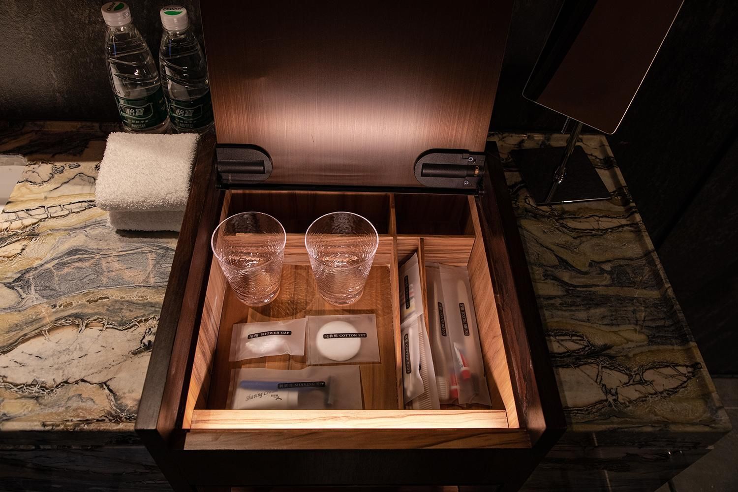 A wooden chest with two glasses, a cotton set, and a shower cap.