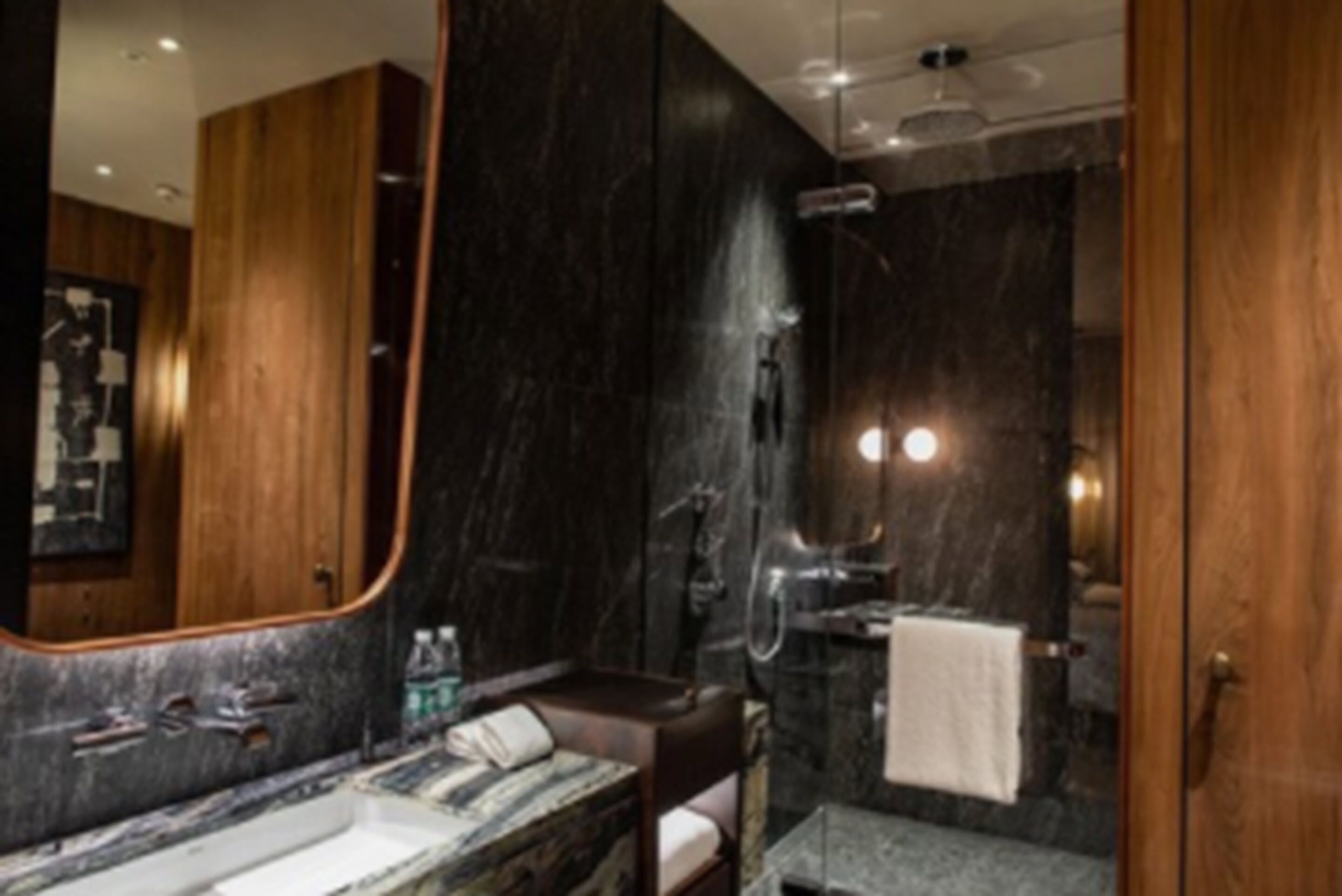 A modern bathroom with a large mirror, a marble sink, a shower, and a wooden vanity.