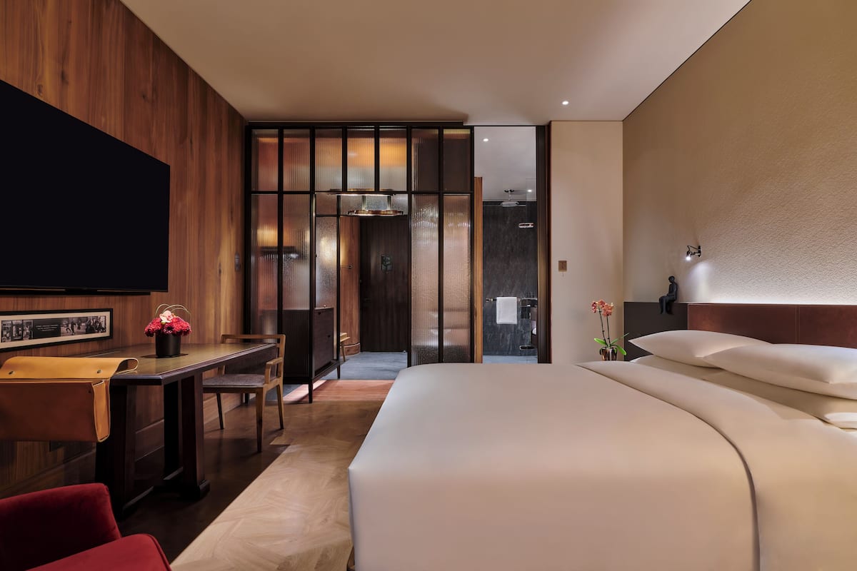 Ein modernes Hotelzimmer mit einem großen Bett, einem Schreibtisch mit Stuhl, einem Flachbildfernseher und einer Schiebetür zu einem Badezimmer.