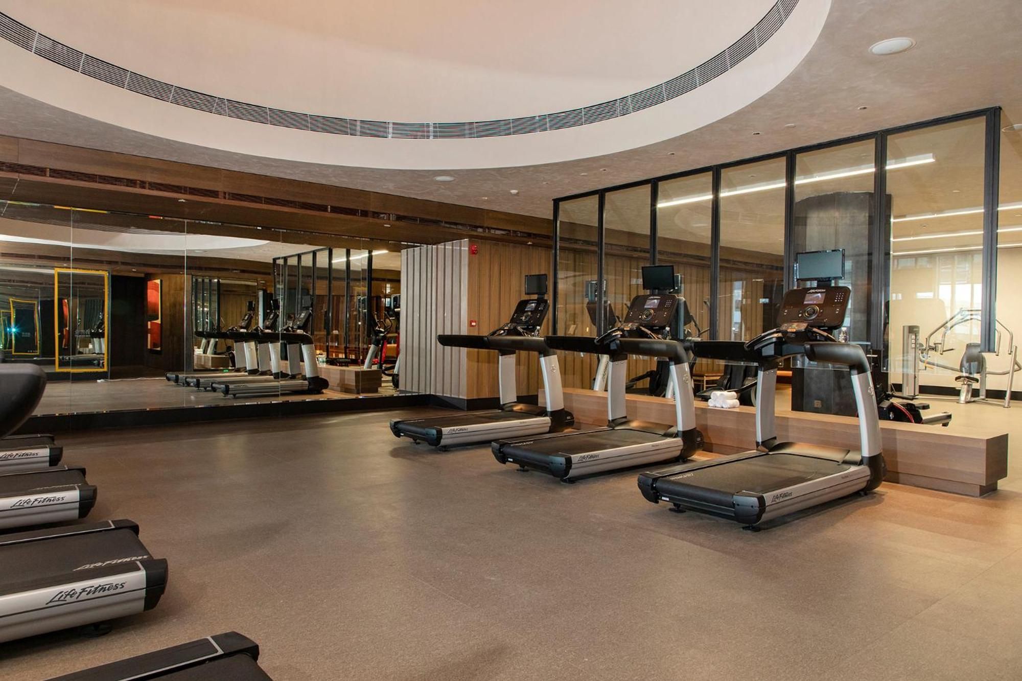 A modern gym with treadmills, exercise bikes, and mirrored walls.