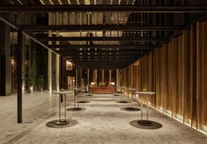 A spacious corridor with a wooden wall on one side and a glass wall on the other, featuring round tables and chairs. - Mumian Beijing Daxing International Airport, part of Hyatt (Daxing)