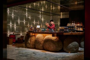 Un bar con un cantinero, una base de piedra y una pared llena de botellas.