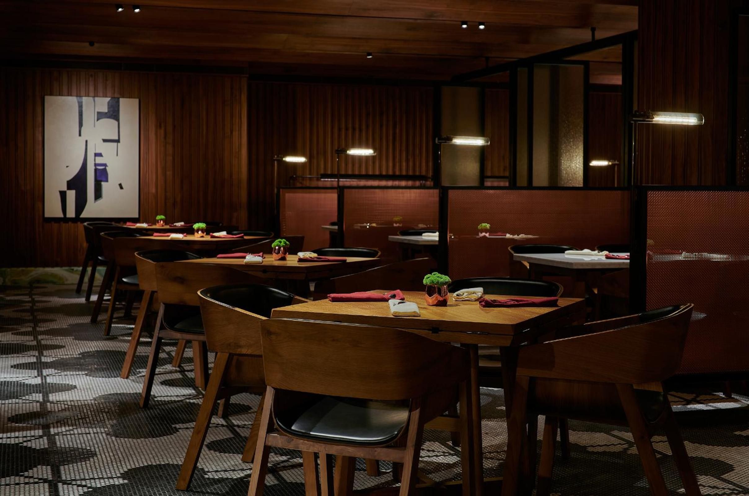 A restaurant interior with wooden tables and chairs, a large abstract painting on the wall, and a patterned carpet.