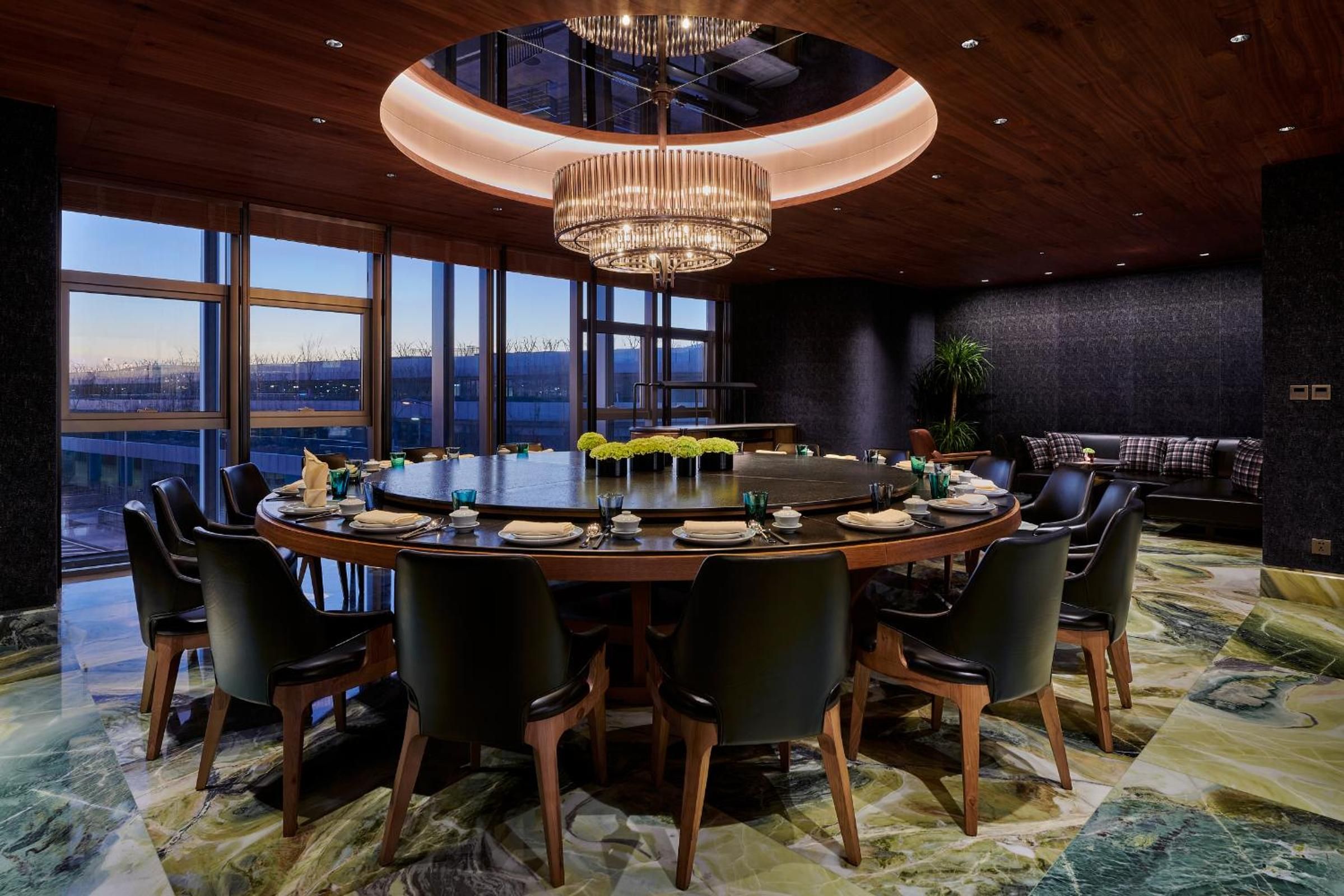 A conference room with a round table, black chairs, a chandelier, and large windows with a view.
