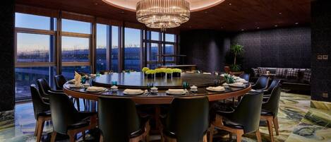 A conference room with a round table, black chairs, a chandelier, and large windows with a view.
