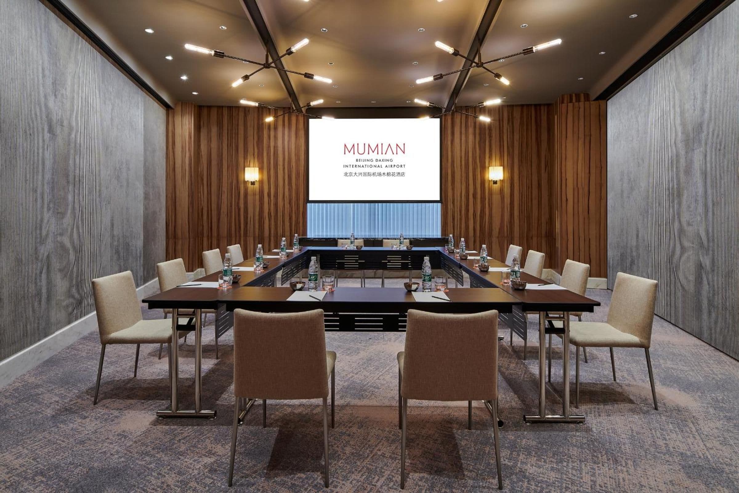 A conference room with a long table, chairs, and a large screen displaying text.