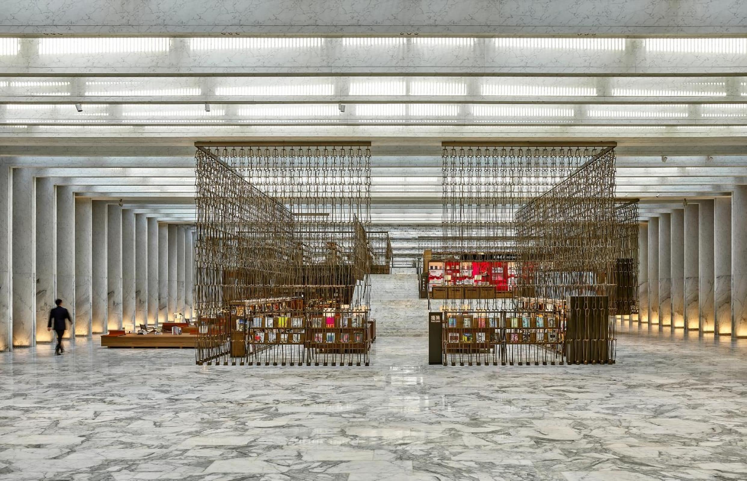 Eine großzügige Lobby mit Marmorböden und modernem Design, mit zwei zentralen Vitrinen voller Bücher und einer Person, die sich dort bewegt.