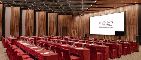 A conference room with rows of tables, red chairs, and a large screen displaying 'MUMIAN' text.