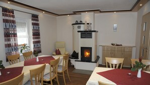 A dining area with wooden chairs and tables, a fireplace, and a window with curtains. - Landgasthaus Zum Mönchshof (Wolframs-Eschenbach)