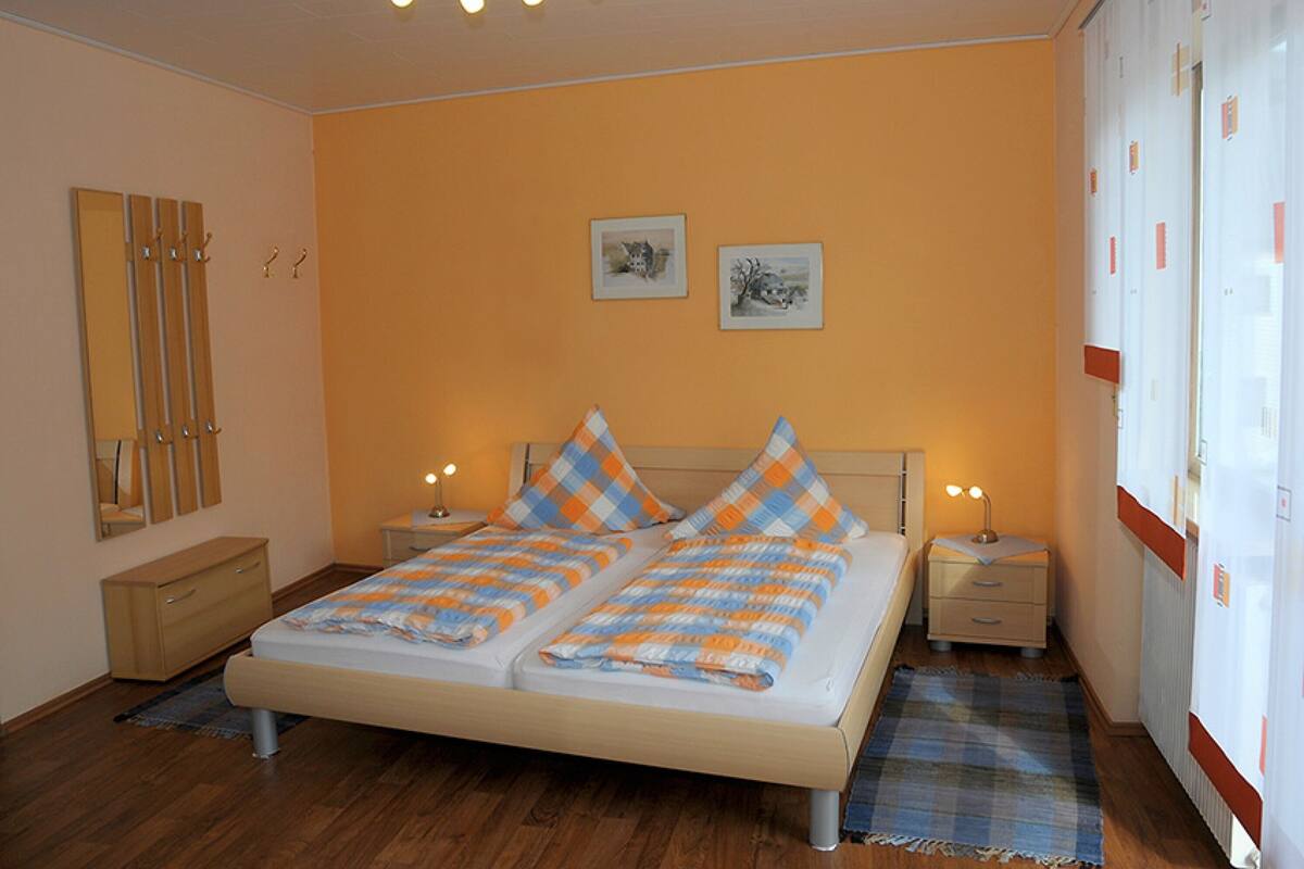 Een slaapkamer met een bed, twee nachtkastjes, een spiegel en twee aan de muur hangende foto's.