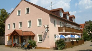 A two-story building with a balcony, a clock, and outdoor seating with umbrellas. - Landgasthaus Zum Mönchshof (Wolframs-Eschenbach)