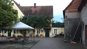 Un patio con suelo de ladrillo, una carpa blanca y un edificio con puerta verde y ventanas.