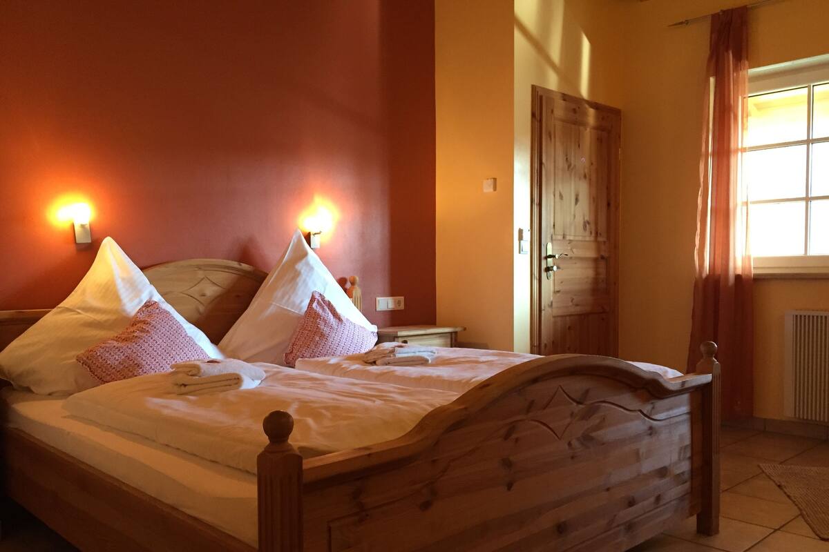 A neatly made bed with pillows and a wooden headboard, a wall-mounted light fixture, and a door with a window to the right.