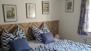 Un dormitorio con una colcha estampada, un cabecero con un panel decorativo y tres cuadros en la pared.