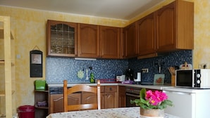 Una cocina con armarios de madera, salpicadero de azulejos, un microondas y una mesa con mantel floral.