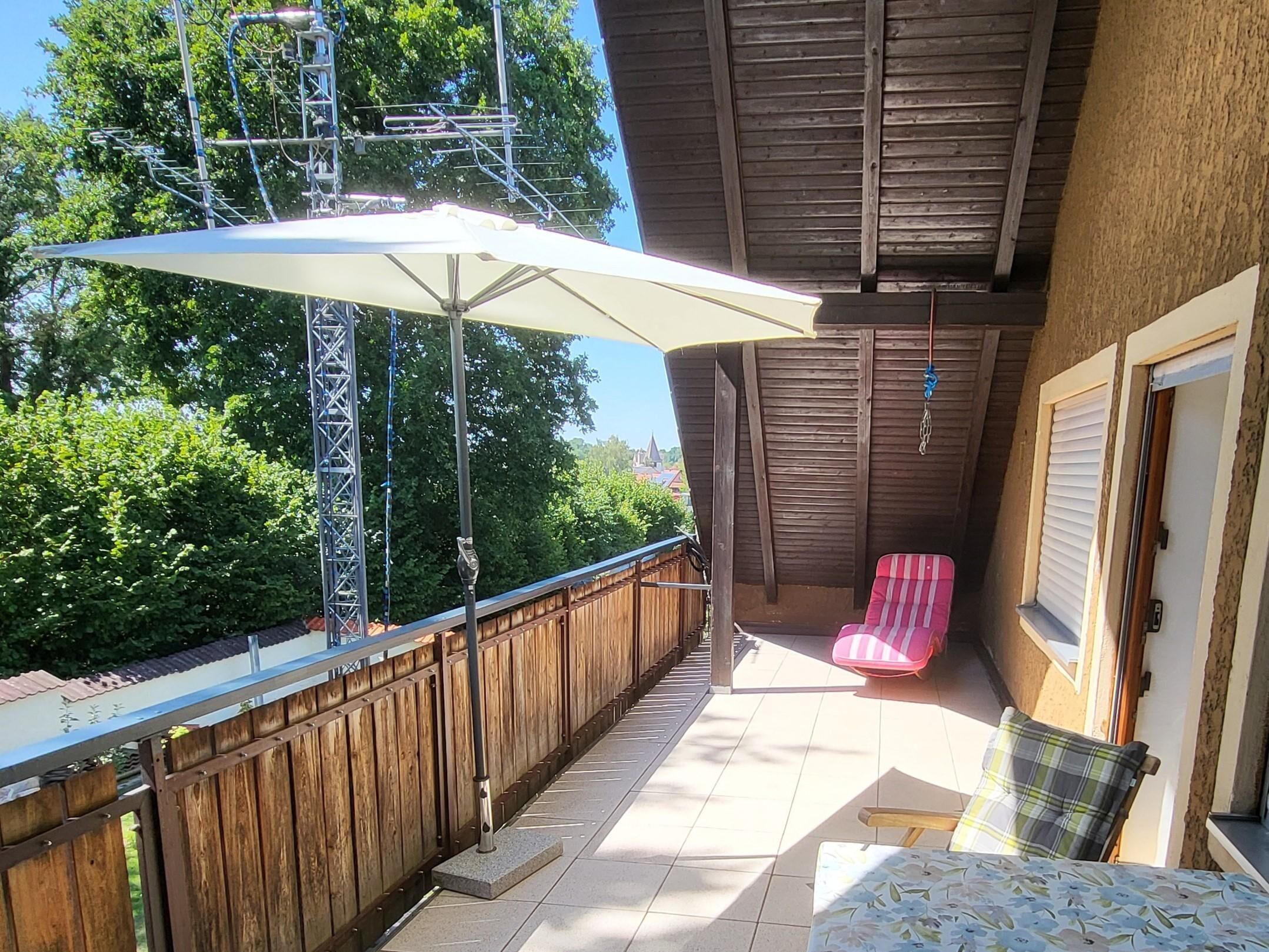 A covered outdoor patio with a wooden fence, a metal structure, and a red chair.