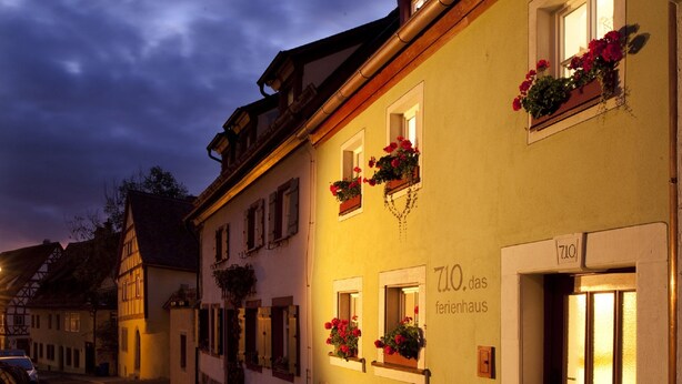 Un edificio tradicional europeo con jardineras en las ventanas, un letrero que indica '710 das ferienhaus' y una puerta con paneles de vidrio esmerilado.