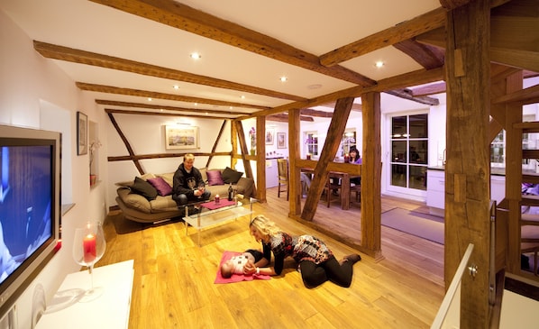 A spacious living area with exposed wooden beams, a television, and a glass coffee table.
