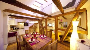 Un comedor con una mesa de madera dispuesta para cuatro personas, rodeada de sillas de madera. Una escalera con vigas de madera conduce a un nivel superior.