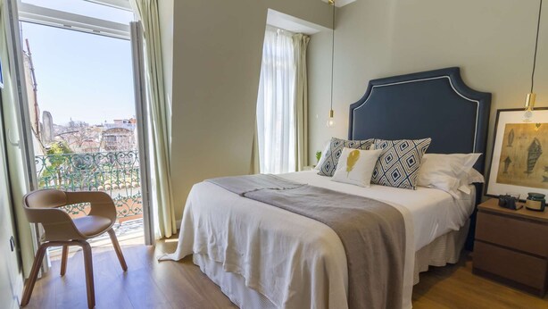 Ein Hotelzimmer mit Bett, Stuhl, Nachttisch und Blick auf die Stadt.