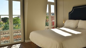 Ein Schlafzimmer mit einem großen Bett, Blick durch ein Fenster und einem Balkon mit Geländer.
