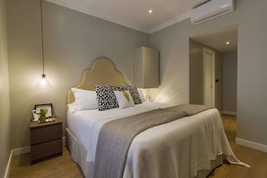 A bedroom with a bed, bedside table, lamp, and an air conditioning unit.