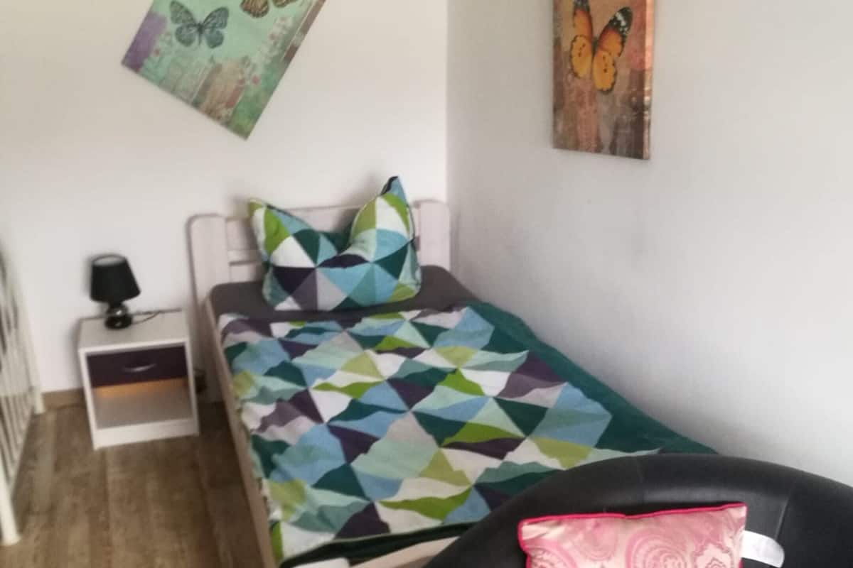 Een slaapkamer met een bed, nachtkastje, stoel en twee kunstwerken aan de muur.