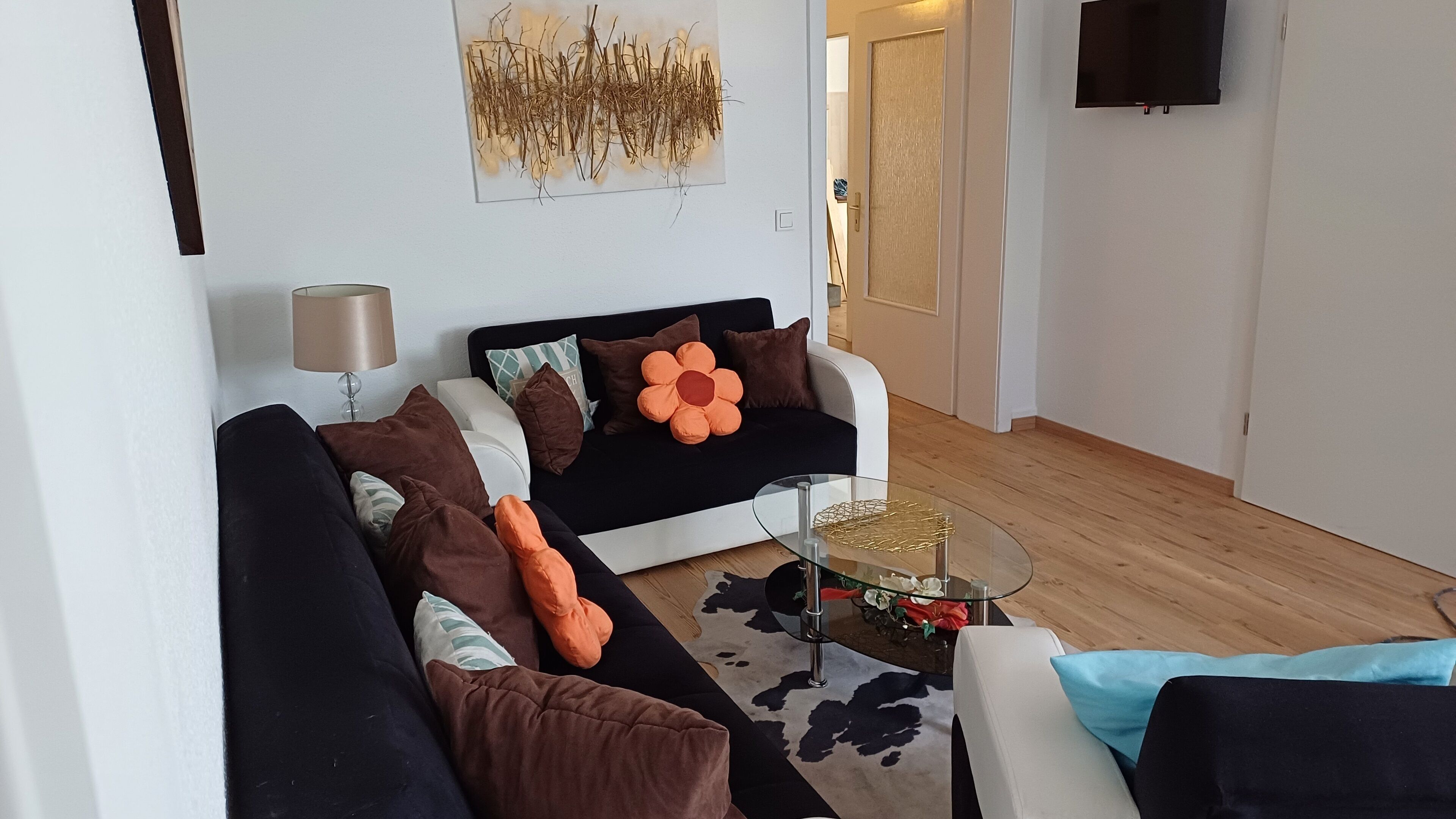 Una sala de estar moderna con un sofá blanco y negro, una mesa de centro de vidrio y un televisor montado.