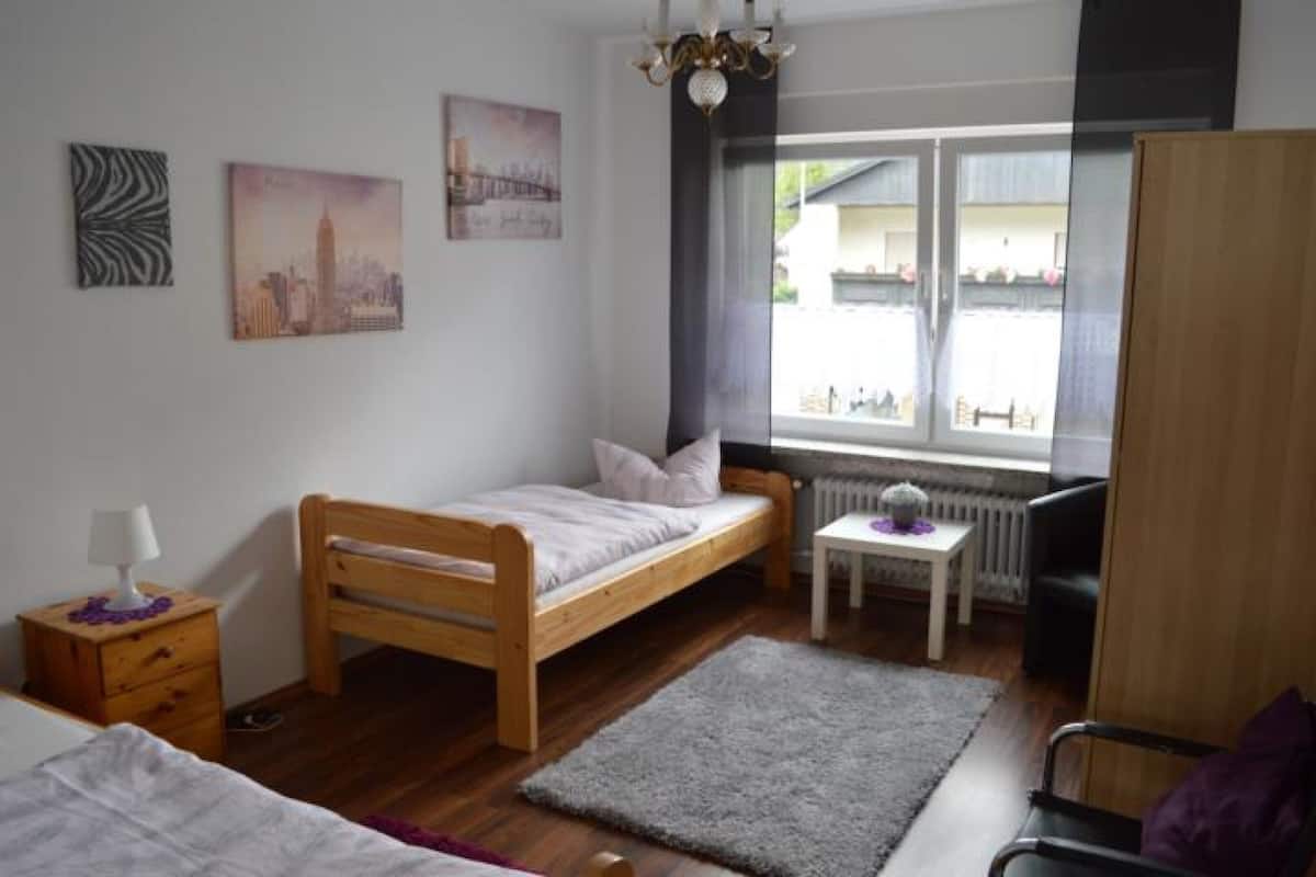 Een kleine, verzorgde slaapkamer met een enkel bed, een nachtkastje, een klein tafeltje en een radiator.