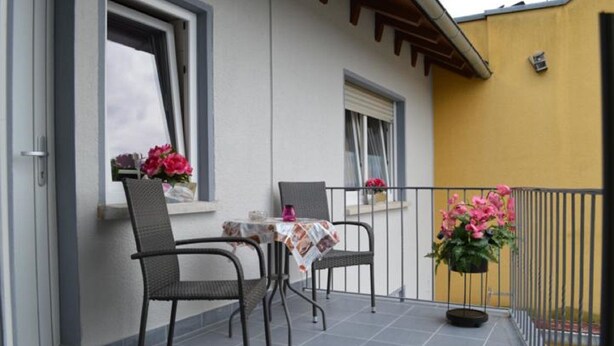 A balcony with two chairs and a table, a potted plant, and a yellow wall. - Ferienwohnungen Stadler (Roedental)