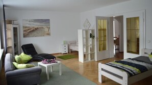 A modern bedroom with a bed, a sofa, a desk, and a wardrobe. - Ferienwohnungen Stadler (Roedental)