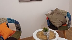A room with a large painting of a bridge, two chairs with patterned cushions, and a small table with a plant. - Ferienwohnungen Stadler (Roedental)