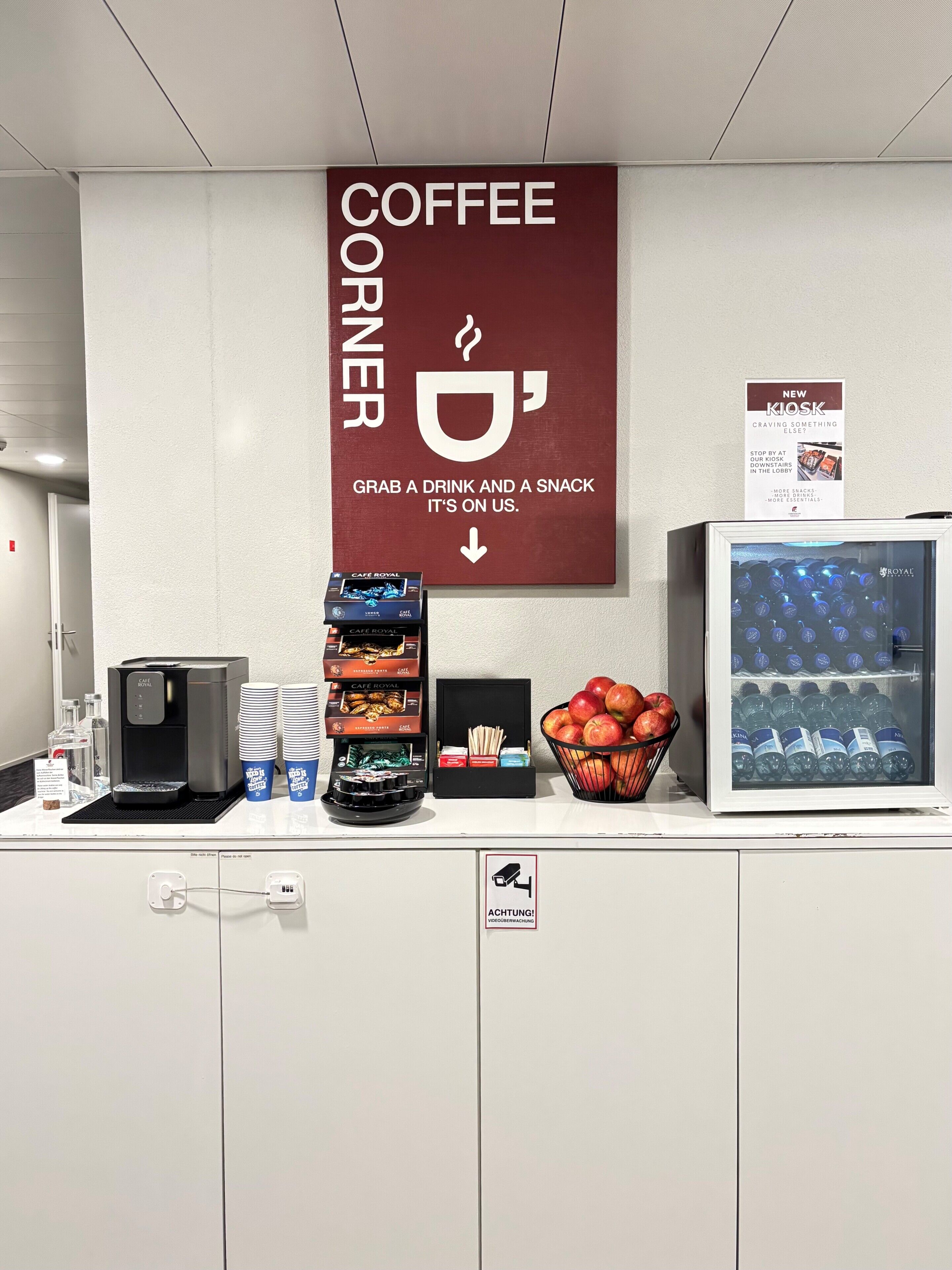 A coffee station with a coffee machine, cups, snacks, and a water dispenser.