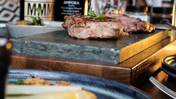 A steak on a wooden board, a bottle of Amfora wine, and a glass of red wine on a table.